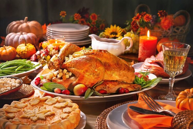 Thanksgiving dinner. Roasted turkey garnished with cranberries on a rustic style table decoraded with pumpkins, vegetables, pie, flowers, and candles