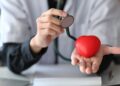 Doctor with stethoscope holding red heart in his hand. Healthcare and medical concept.