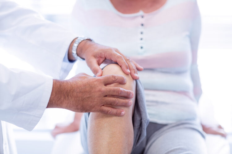 Physiotherapist giving knee therapy to senior woman in clinic