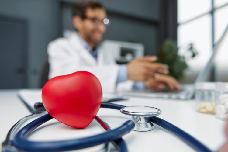 Stethoscope, red heart and cardiogram on gray table. Cardiology concept