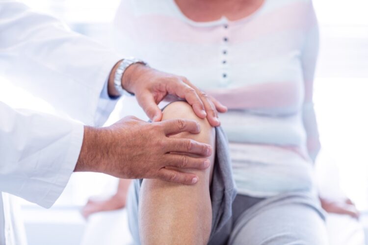 Physiotherapist giving knee therapy to senior woman in clinic